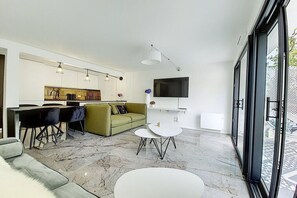 A modern living room with a sofa, dining area, and a TV mounted on the wall.