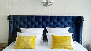 Una cama con cabecera capitonada, almohadas blancas y amarillas, y una lámpara de pared.