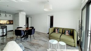 Una sala de estar moderna con comedor, un sofá con almohadones decorativos y una alfombra blanca y mullida.