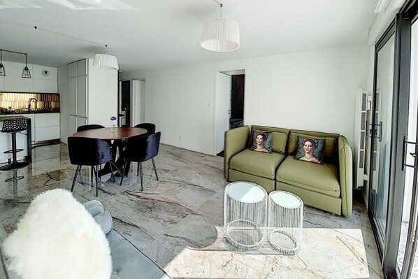 A modern living room with a dining area, a sofa with decorative pillows, and a white furry rug.