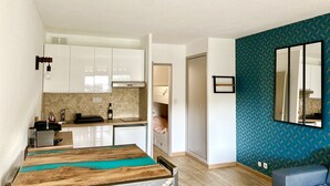 Ett kompakt bostadsutrymme med ett litet kök, en matplats med ett träbord och en blå, mönstrad vägg.
