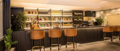 Una zona de bar con mostrador, varias estanterías llenas de botellas y taburetes.