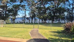 A grassy area with a metal fence, a paved path, and trees. - Peaceful Waterfront by Book Jervis Bay - wheelchair accessible - Stunning Location for Family Holiday (Sanctuary Point)