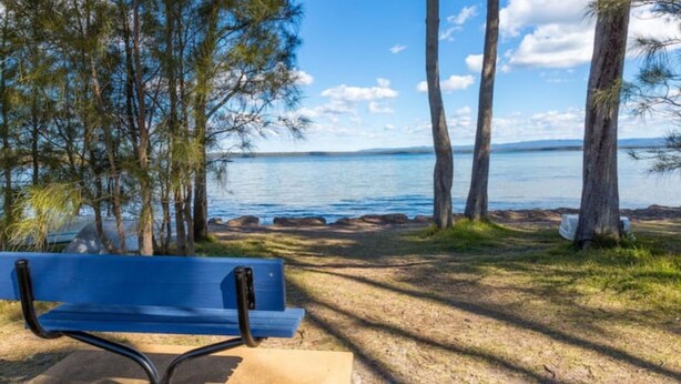 A bench by a lakeside with trees and a clear view of the water. - Peaceful Waterfront by Book Jervis Bay - wheelchair accessible - Stunning Location for Family Holiday (Sanctuary Point)