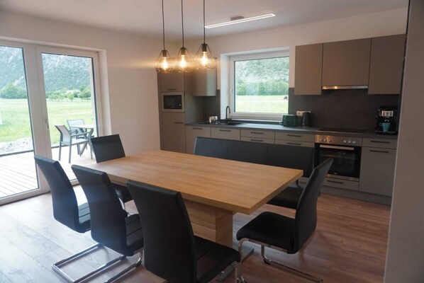 A modern kitchen with a wooden dining table, black chairs, and a built-in oven.