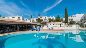 A swimming pool with blue water, surrounded by white buildings with balconies and trees. - Carolina Sea Apartment By Dreamplaces (Albufeira)