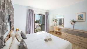A hotel room with a bed, a desk, a dresser, and a balcony with curtains. - Carolina Sea Apartment By Dreamplaces (Albufeira)