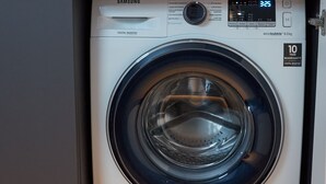 Un lave-linge à variateur de vitesse numérique de la marque Samsung, installé dans une cuisine dotée d’un pare-feu en marbre et d’un plan de travail en bois.