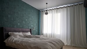 Une chambre avec un grand lit, des murs de couleur turquoise et une fenêtre ornée de rideaux blancs.