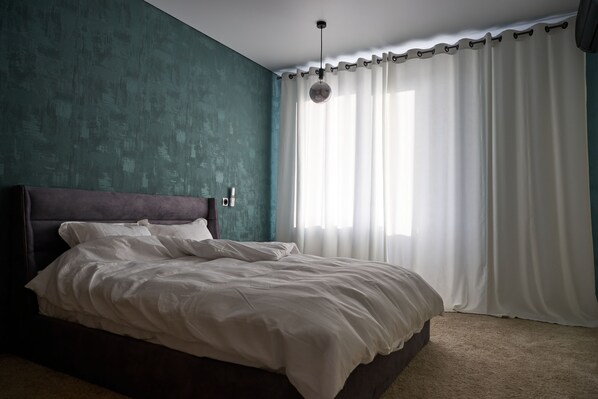 A bedroom with a large bed, teal walls, and a window with white curtains.