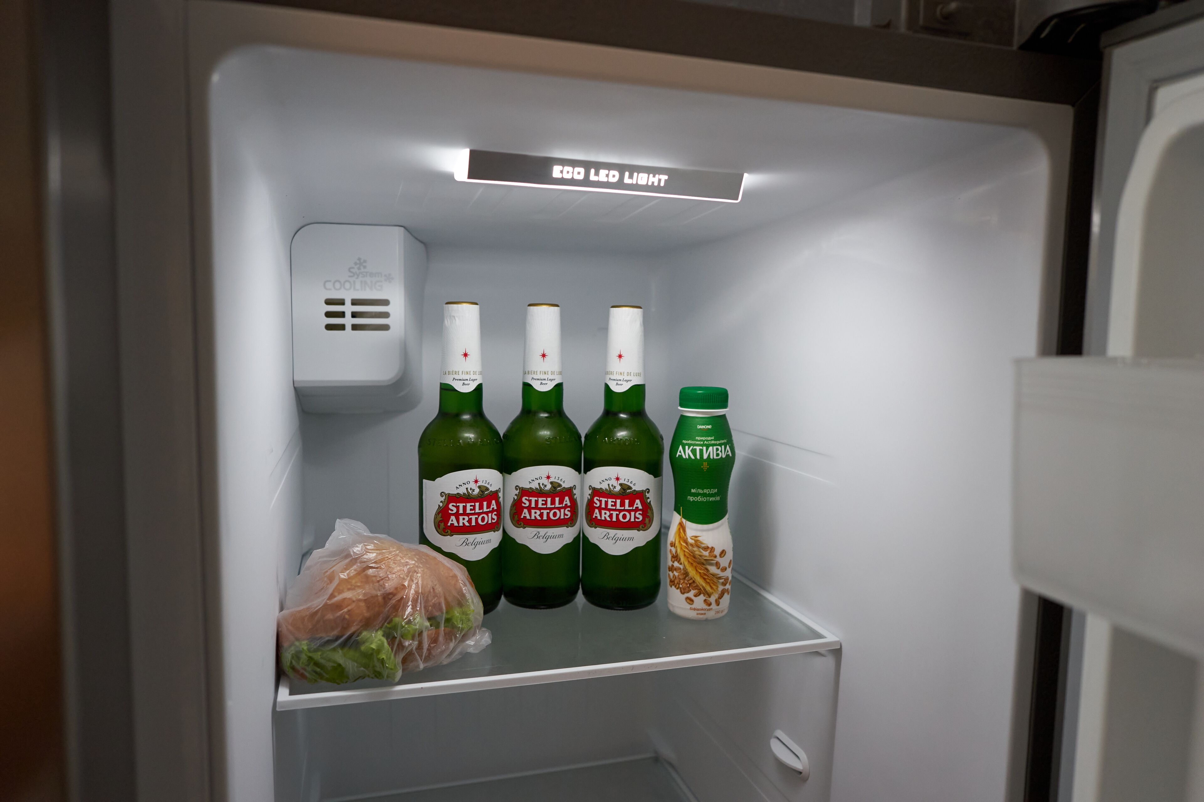 Un refrigerador con cuatro botellas de cerveza Stella Artois y una botella de yogur Activia.