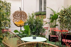 Un espacio al aire libre acogedor con mobiliario de mimbre, una silla colgante y plantas en macetas.