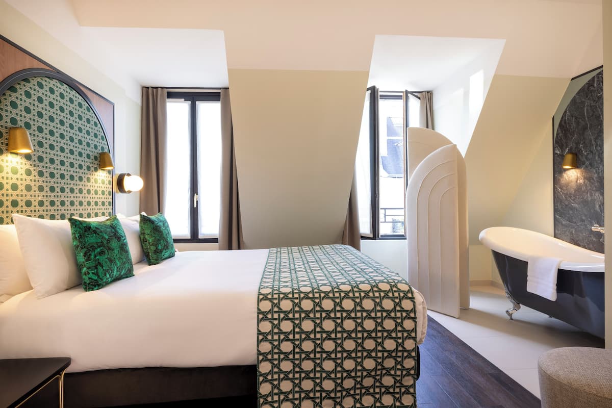 Habitación de hotel con una cama grande, una bañera y un espejo.