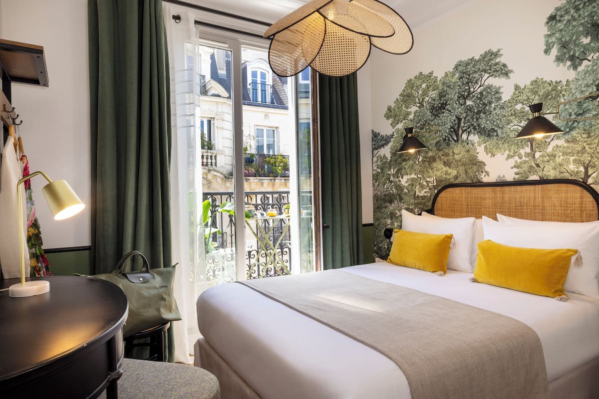 Habitación de hotel con cama, escritorio, lámpara y vista a un balcón.