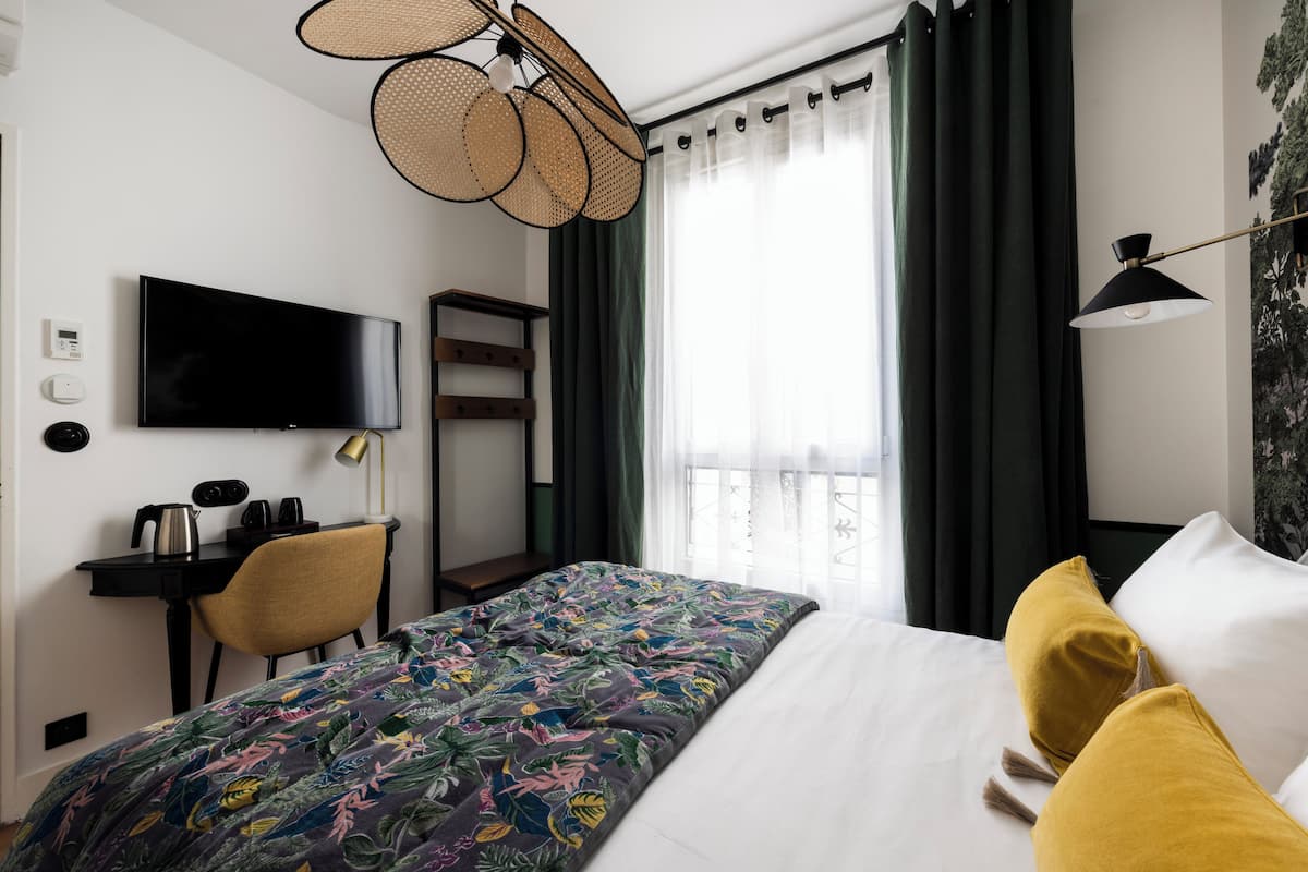 Habitación de hotel con cama, escritorio, silla, televisión y ventana con cortinas.