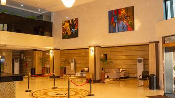A hotel lobby with a reception desk, seating area, artwork on the walls, and a chandelier.