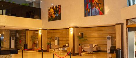 A hotel lobby with a reception desk, seating area, artwork on the walls, and a chandelier.