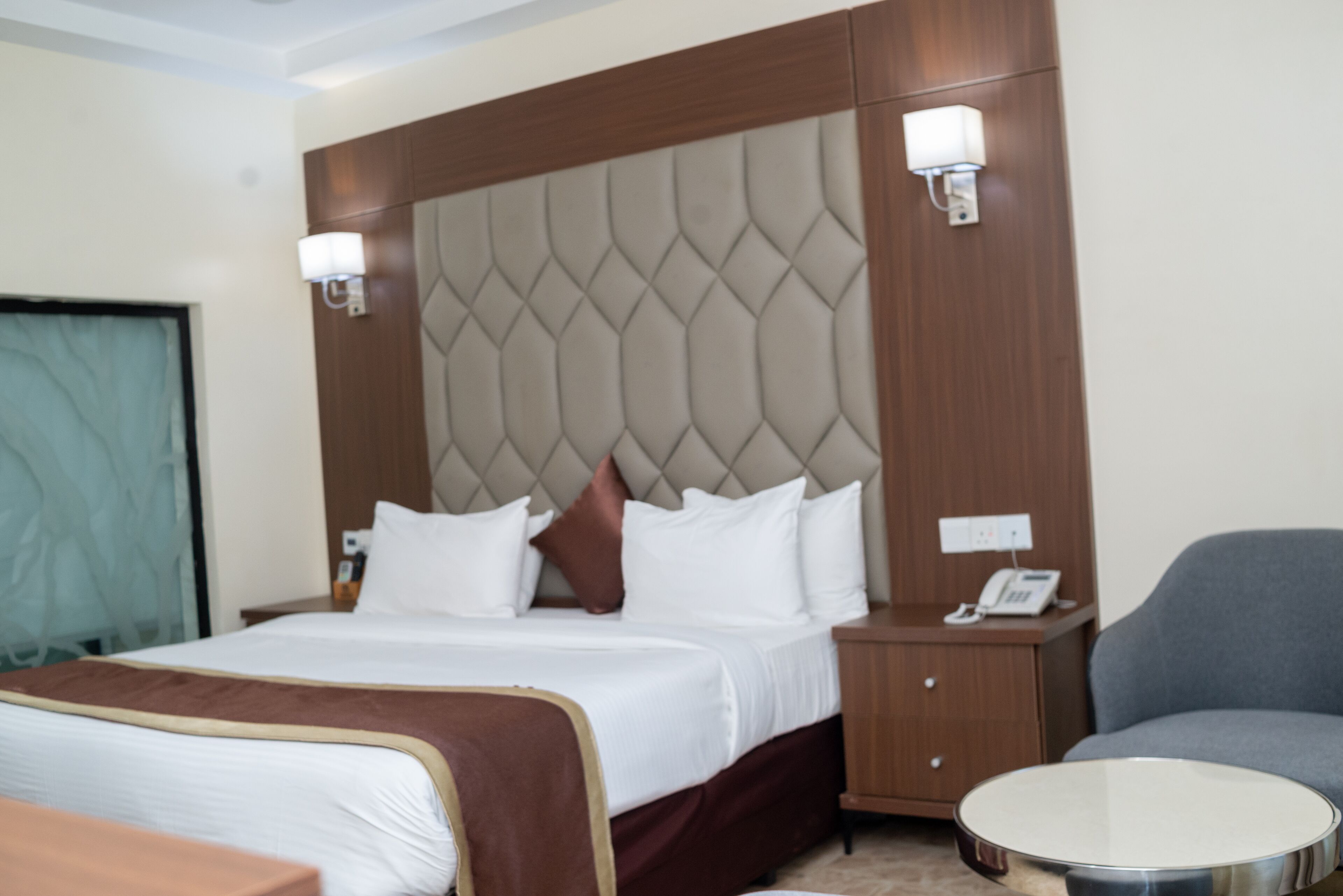 Een hotelkamer met een groot bed, een nachtkastje met een telefoon, een ronde tafel en een stoel.