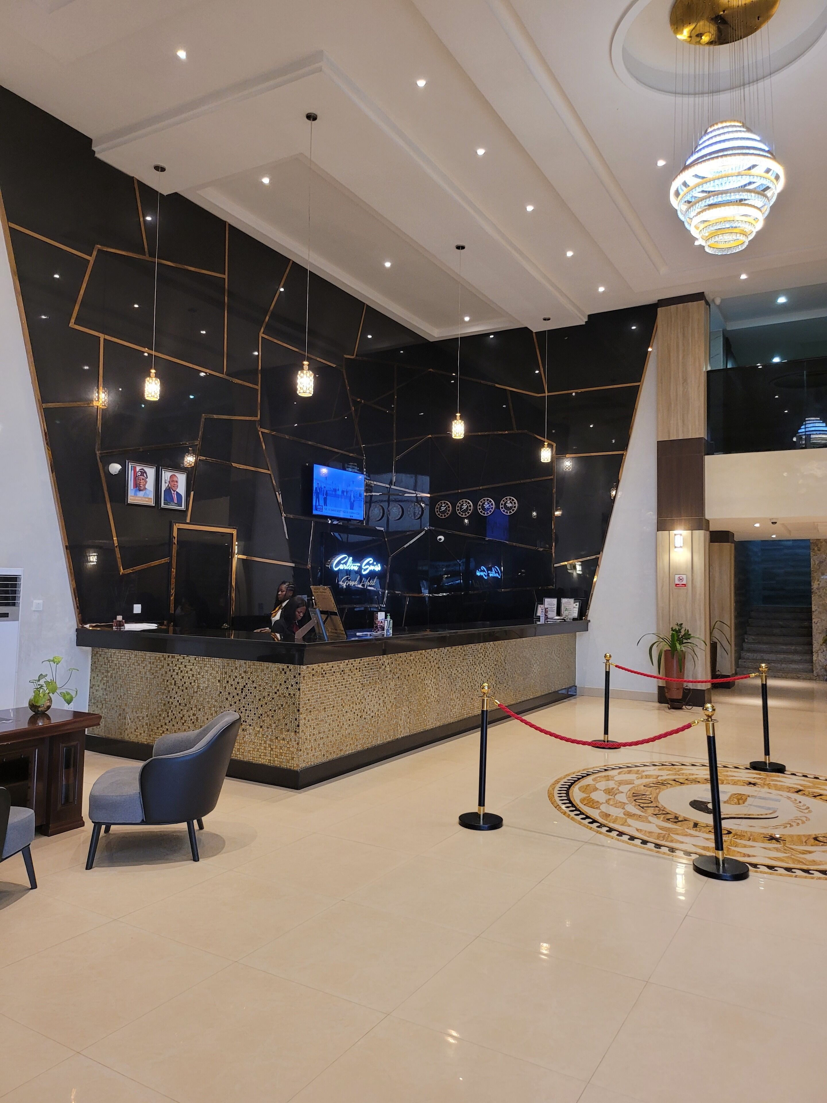 A modern reception area with a black and gold geometric wall design, a reception desk, and a chandelier.