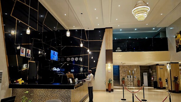 Een moderne hotellobby met een receptiebalie, een grote kroonluchter en een hoog plafond met ingebouwde verlichting.