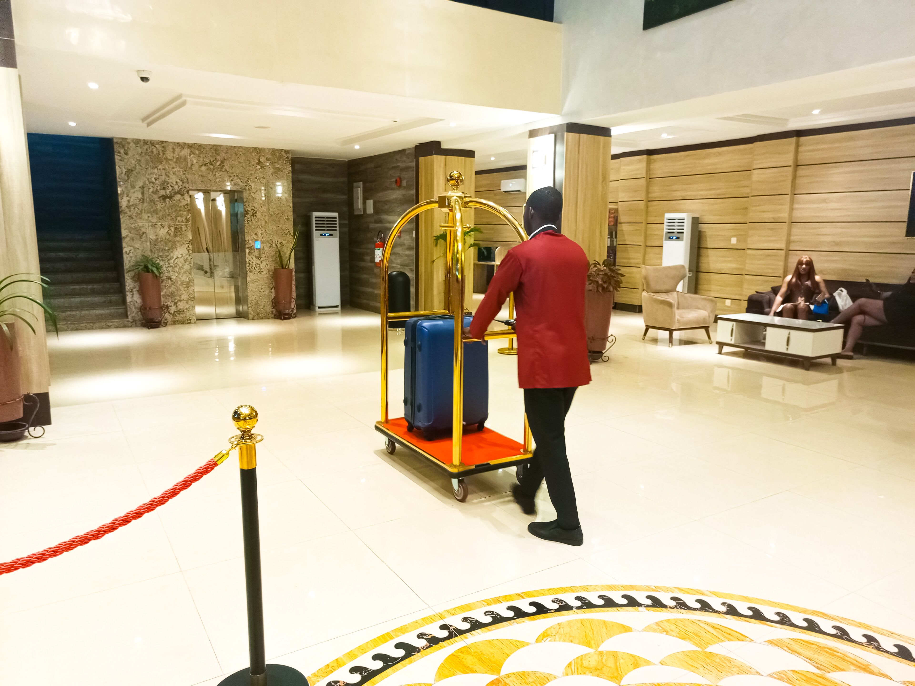 Um saguão de hotel com parede de mármore, balcão de recepção e área de estar com um sofá e poltronas.
