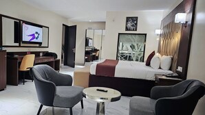 Een hotelkamer met een bed, twee fauteuils, een bureau, een televisie en een spiegel.