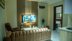 Een woonkamer met een bank, een televisie en een salontafel met glazen en een fles.