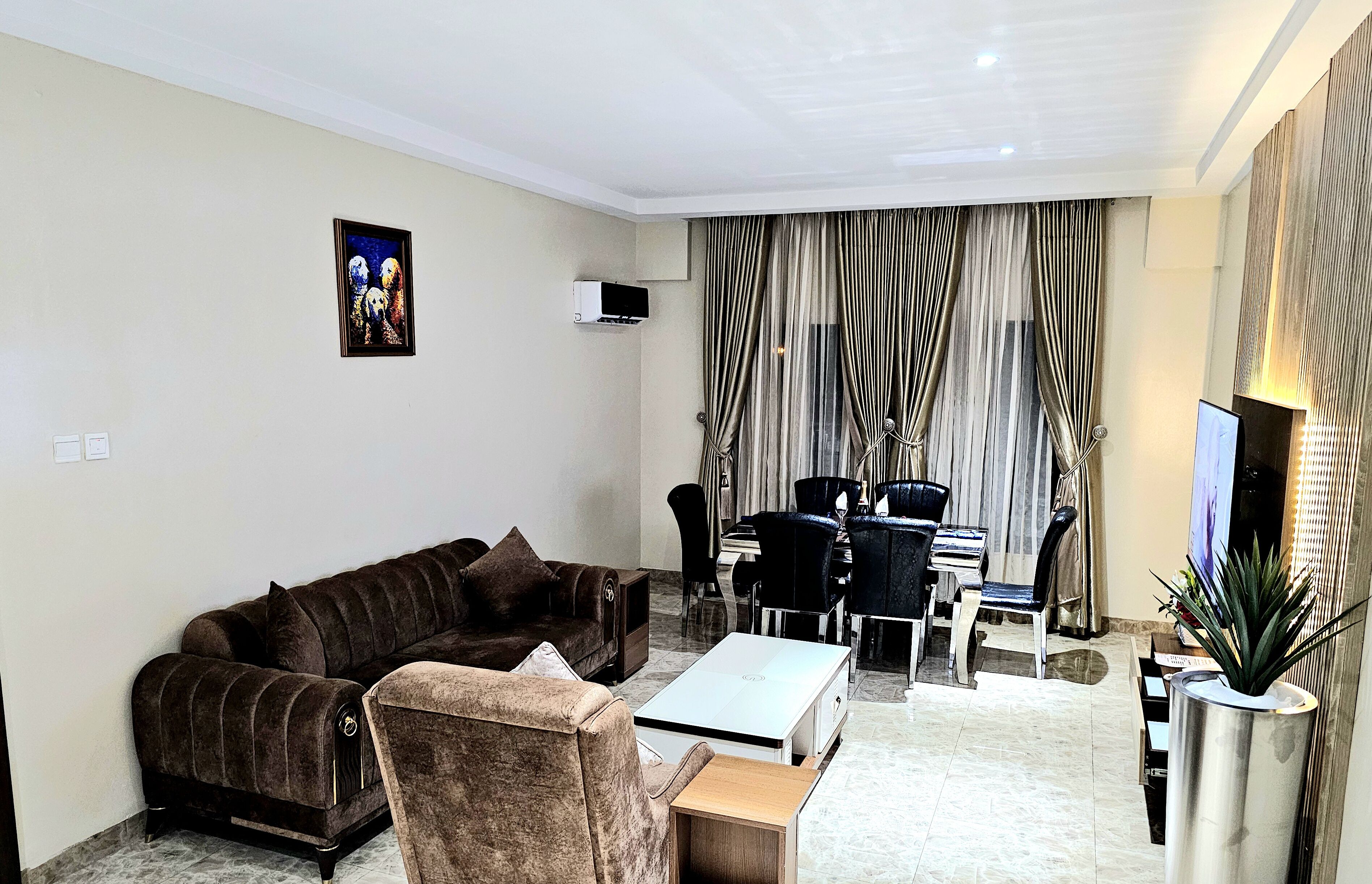 A modern living room with a sectional sofa, a coffee table, a TV, and a dining area with chairs and a table.