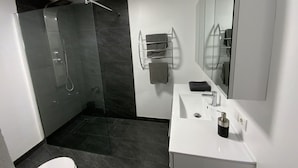 A modern bathroom with a glass-enclosed shower, a white sink, and a large mirror. - Apartment Business (Imsterberg)