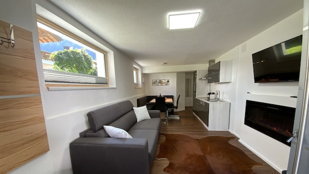 A modern living area with a sofa, a flat-screen TV mounted on the wall, a fireplace, and a cowhide rug. - Apartment Business (Imsterberg)