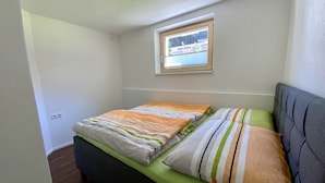 A small, single-bed room with a window, a green bedspread, and a grey headboard. - Apartment Business (Imsterberg)