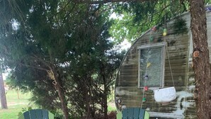 Two green Adirondack chairs on a stone patio with a rustic wooden structure in the background. - The Green Egg - Vintage RV Glamping (Terrell)