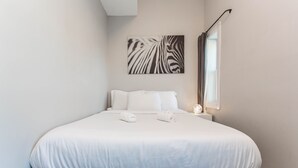 A neatly made bed with white linens and two towels, a zebra print artwork on the wall, and a window with curtains. - ❤️ Modern 2BR Apt Right next to Wrigley Field & Transit  (Chicago)
