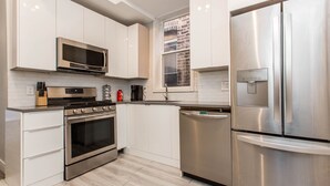 A modern kitchen with stainless steel appliances, white cabinetry, and a window with a view of a brick building. - ❤️ Modern 2BR Apt Right next to Wrigley Field & Transit  (Chicago)