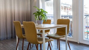 A dining area with a table, four chairs, a potted plant, and large windows with a view of a building. - ❤️ Modern 2BR Apt Right next to Wrigley Field & Transit  (Chicago)