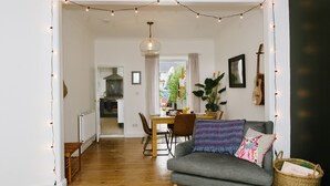 Un salon chaleureux avec un canapé gris, une table à manger avec des chaises, un luminaire suspendu et une guitare accrochée au mur.