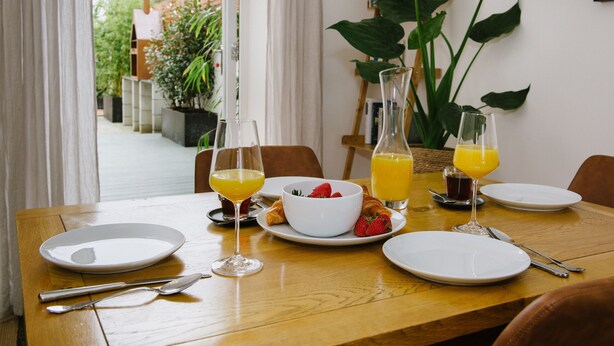 Une table de petit-déjeuner dressée avec des assiettes, des verres et un saladier rempli de fraises et de croissants.