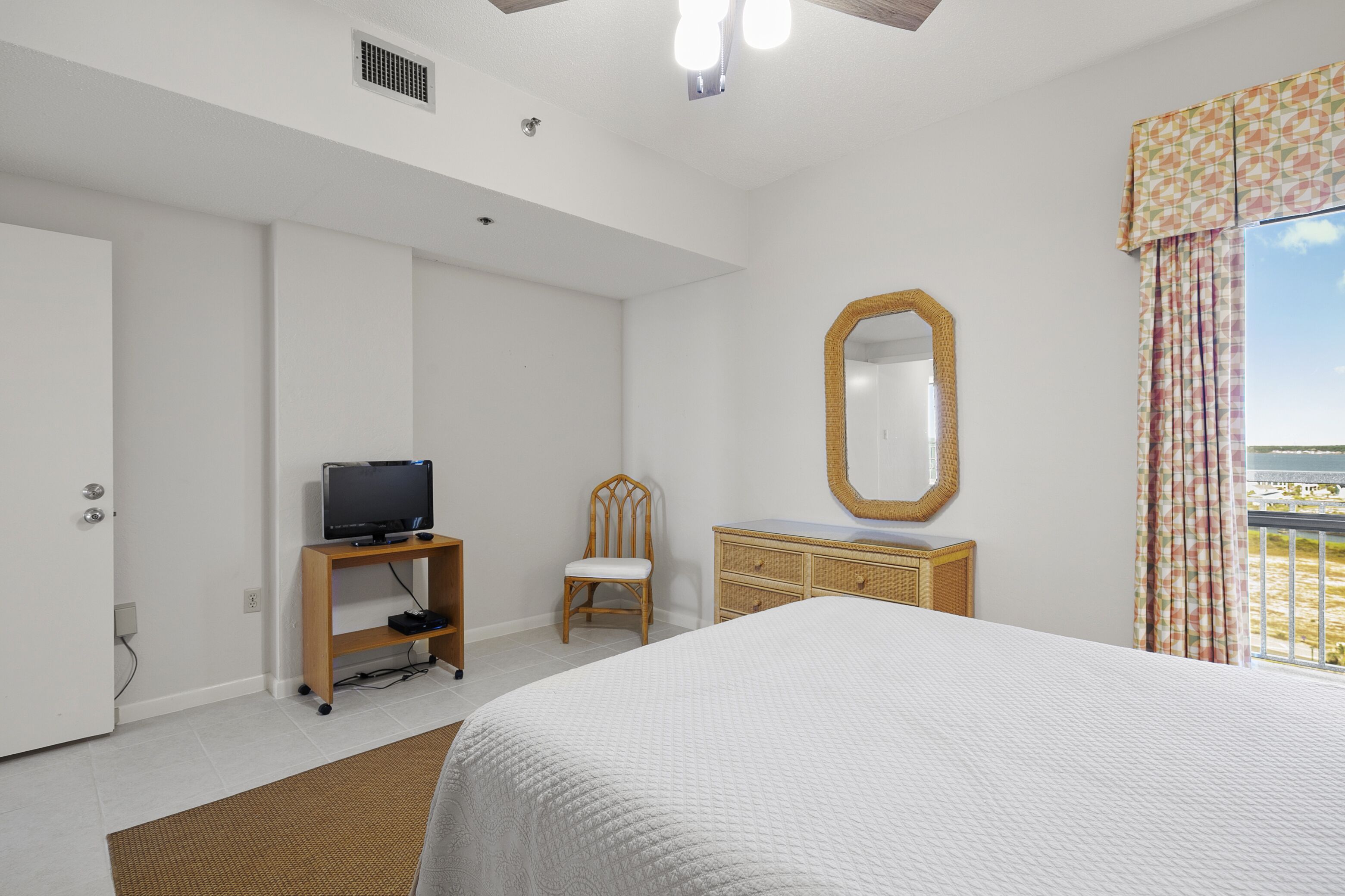 A bedroom with a large bed, a television on a stand, a chair, a dresser, and a window with curtains.