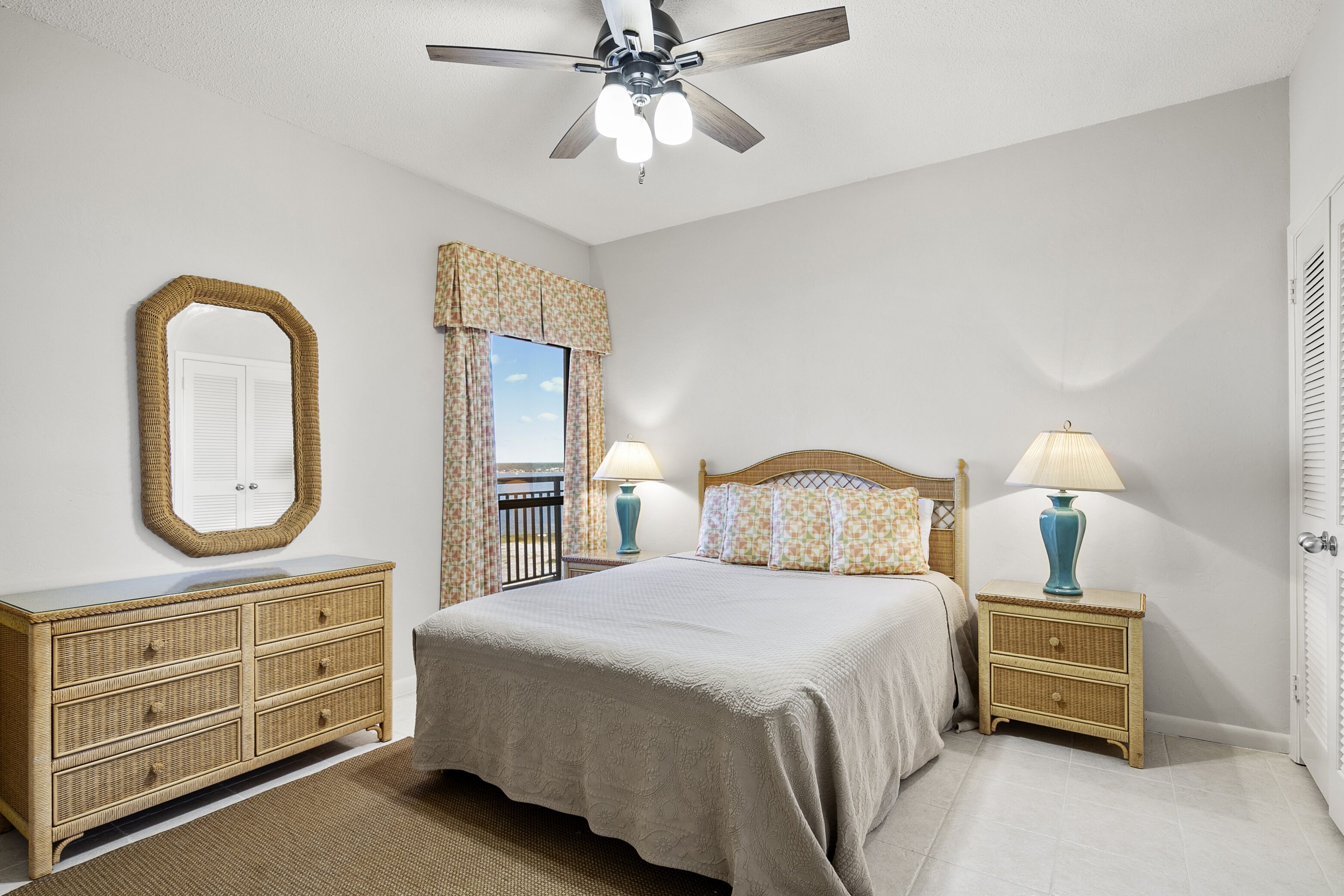 A bedroom with a bed, a dresser, a nightstand, a ceiling fan, and a window with curtains.