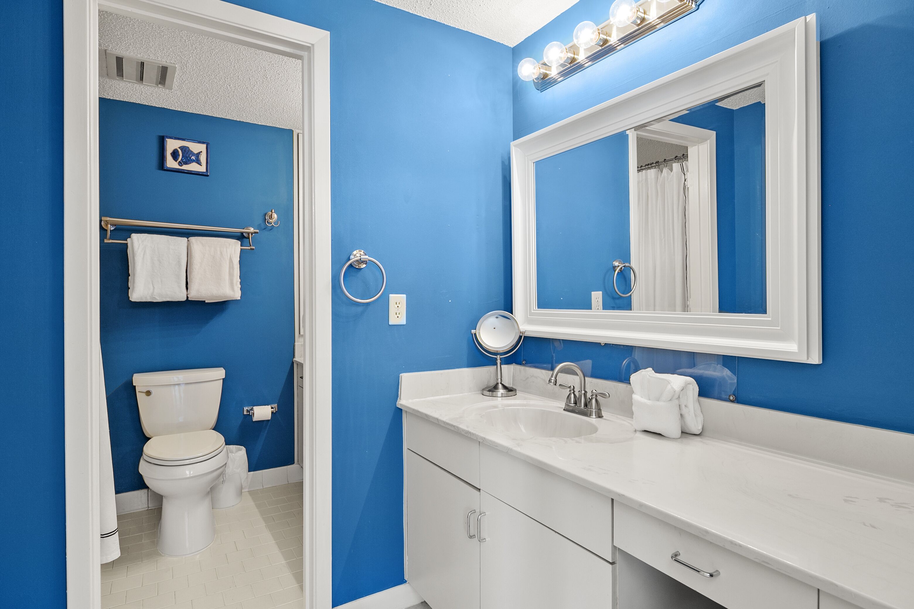 A bathroom with a blue wall, white toilet, and a white sink with a mirror above it.