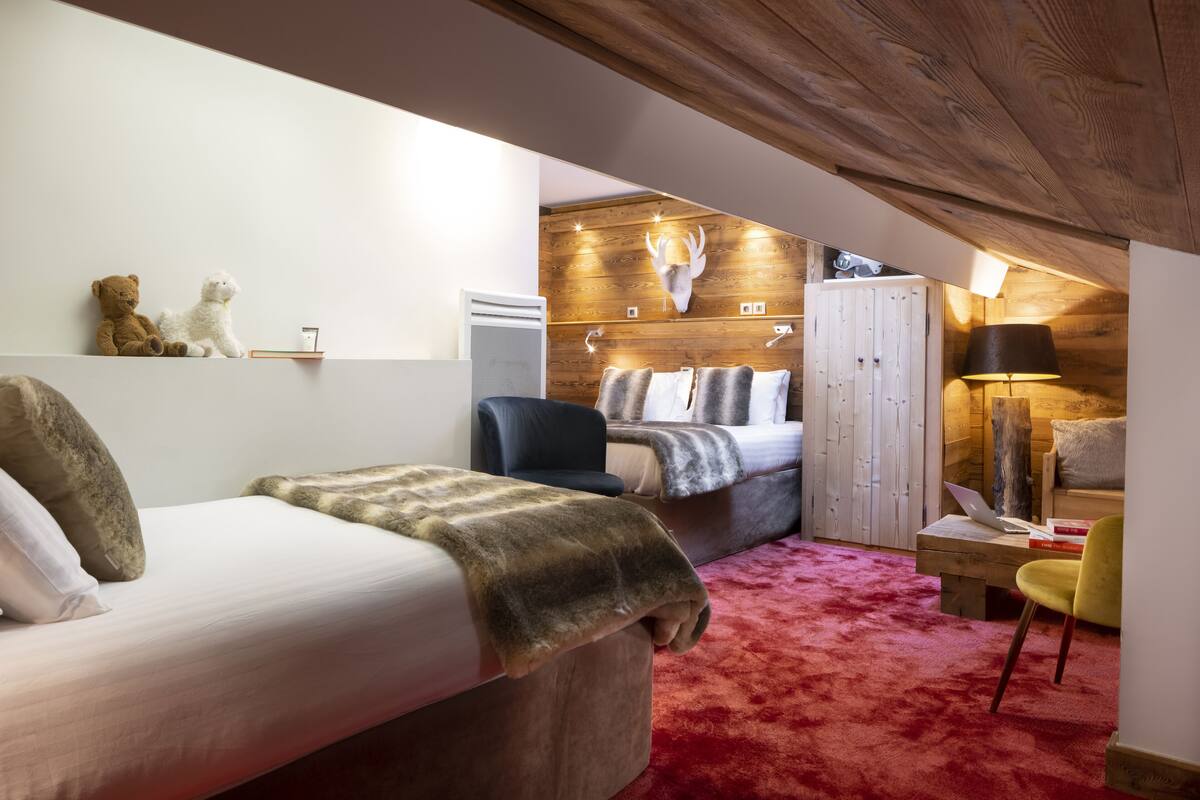A cozy bedroom with a large bed, a desk with a laptop, a chair, and a red carpet.