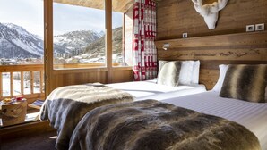 A room with a bed, a mounted deer head, a window with a view of mountains, and a red and white patterned curtain. - Hotel Ski Lodge (Val-d'Isere)