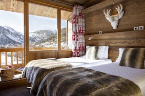 Une chambre avec un lit, une tête de cerf accrochée au mur, une fenêtre donnant sur les montagnes et un rideau rouge et blanc à motifs.
