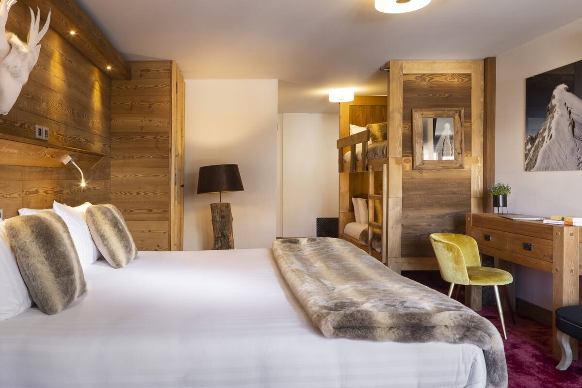 A hotel room with a large bed, wooden walls, a desk, and a chair.