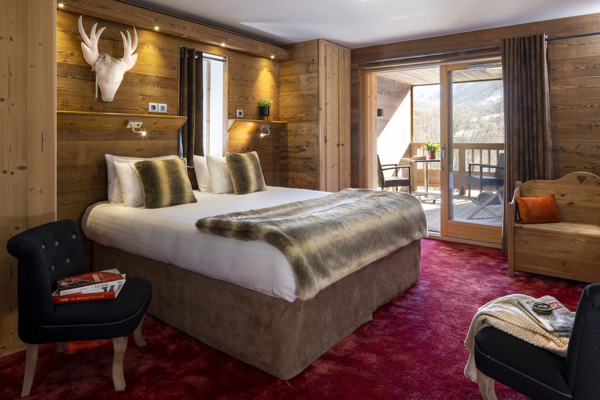 A bedroom with a large bed, wooden walls, a mounted deer head, and a balcony with a view of the outdoors.