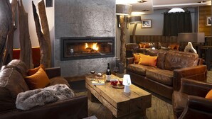 A cozy living room with a fireplace, leather sofas, and a wooden coffee table. - Hotel Ski Lodge (Val-d'Isere)