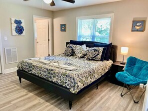 Um quarto com uma cama, uma cadeira azul, uma mesa de cabeceira e uma janela com persianas.