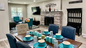A dining area with a brick fireplace, teal tableware, and modern decor. - Modern High Point Getaway | 3BR, HPU & RV Space (High Point)