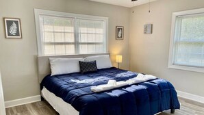 A bedroom with a bed, two windows with blinds, a bedside lamp, and a framed picture on the wall. - Modern High Point Getaway | 3BR, HPU & RV Space (High Point)