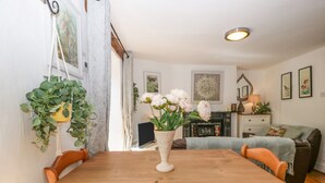 A dining area with a wooden table and chairs, a vase with flowers, and a fireplace in the background. - Mackerel Cottage (Budleigh Salterton)